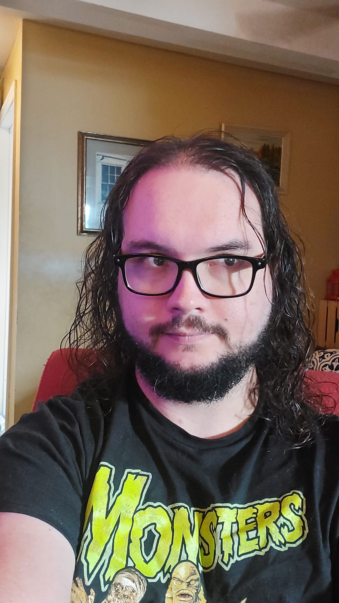 A man with long dark hair and a beard sits in a computer chair, photo 3